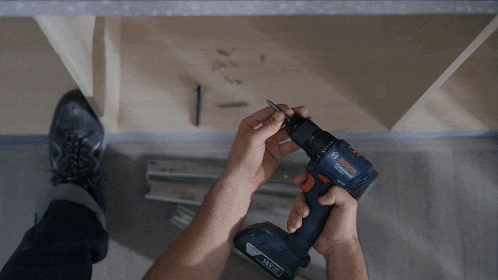A person holds a blue Bosch Professional cordless drill over wood.