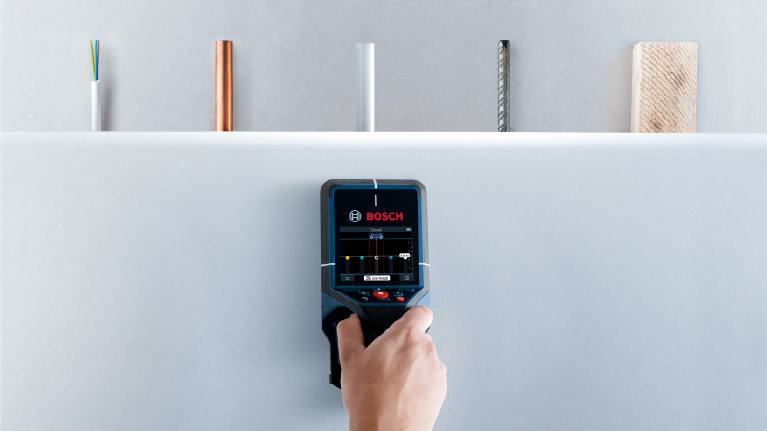 A hand holds a Bosch Professional detection device against a wall.