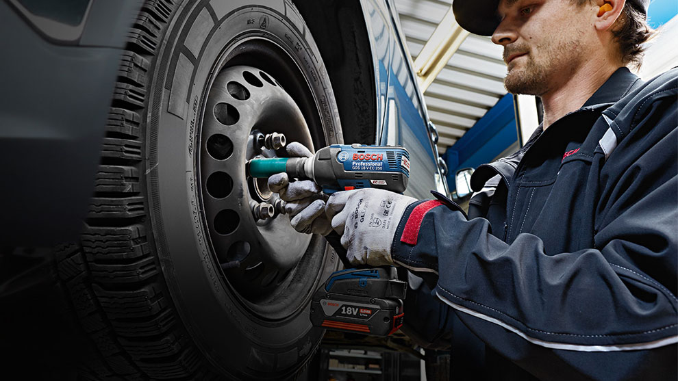 A mechanic is using a Bosch Professional cordless impact wrench on the tire.