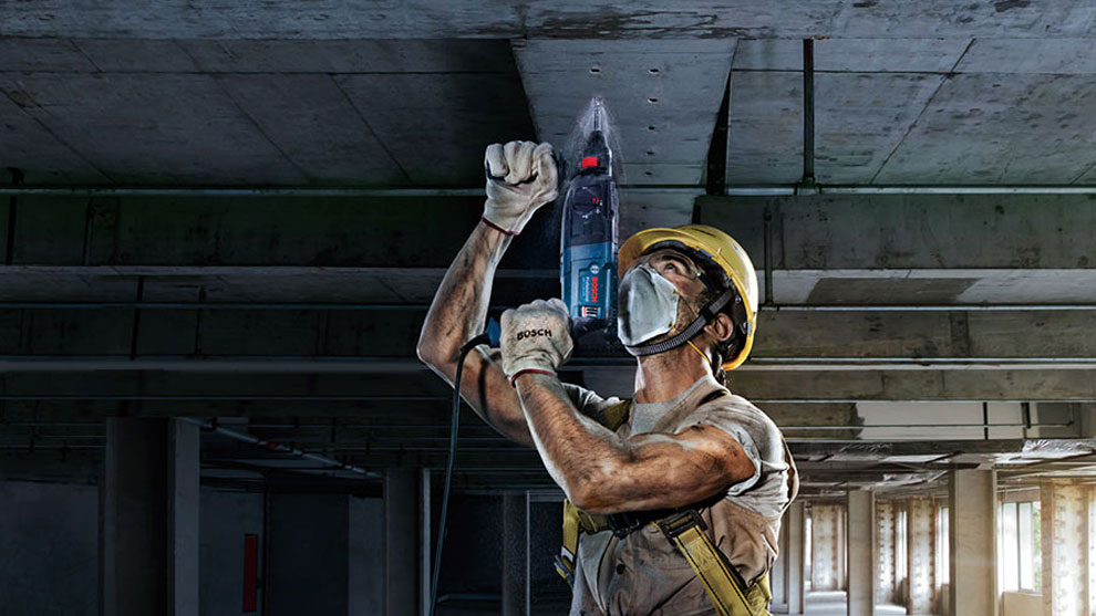 A worker with a yellow helmet is using a Bosch Professional drill.