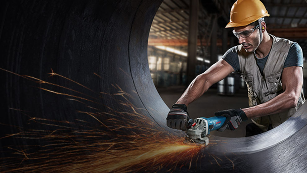 A worker with a helmet is cutting metal with a blue Bosch cutting machine.