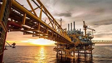 A yellow oil platform rises above the water, with a sunset in the background.