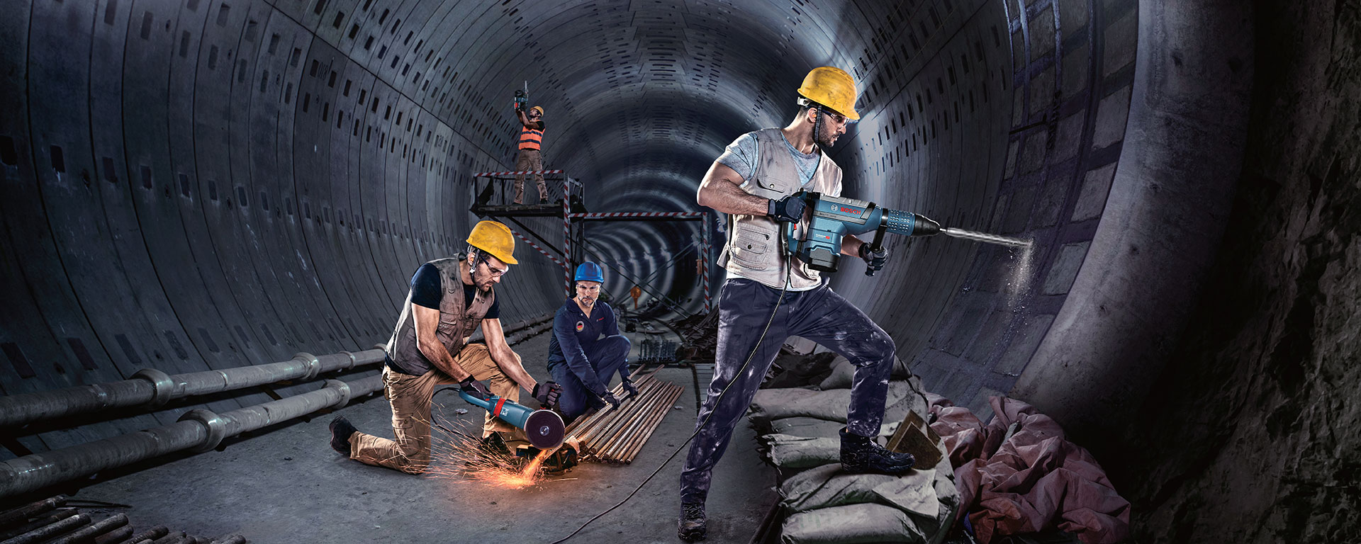 Three construction workers in a tunnel are using Bosch tools. Dust and sparks are flying.