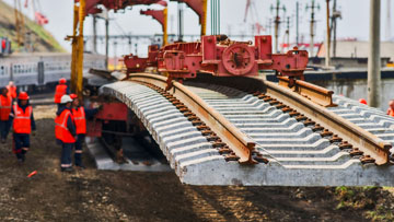 Workers in orange clothing are laying tracks with a crane.