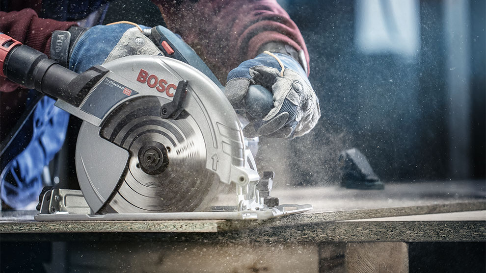 A Bosch Professional circular saw cuts wood, dust swirls up.