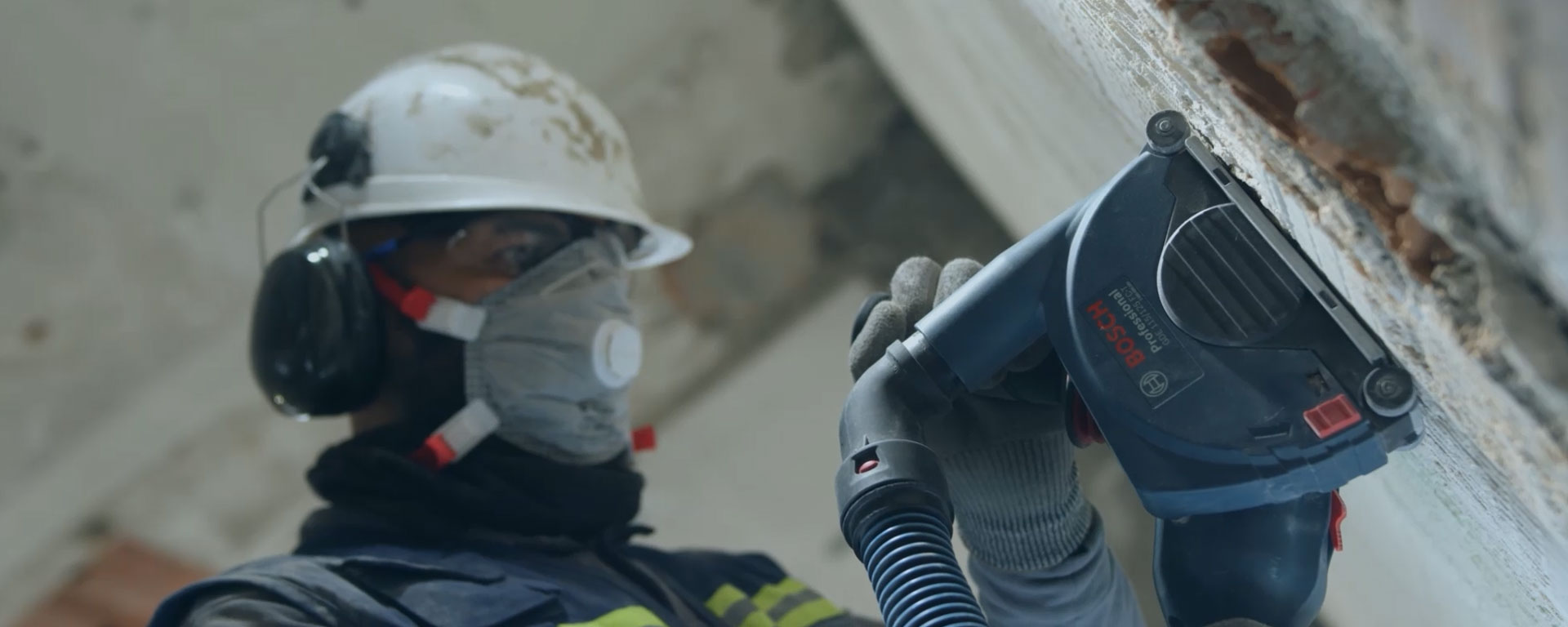 A worker wearing a helmet is using a Bosch Professional tool vacuum cleaner.