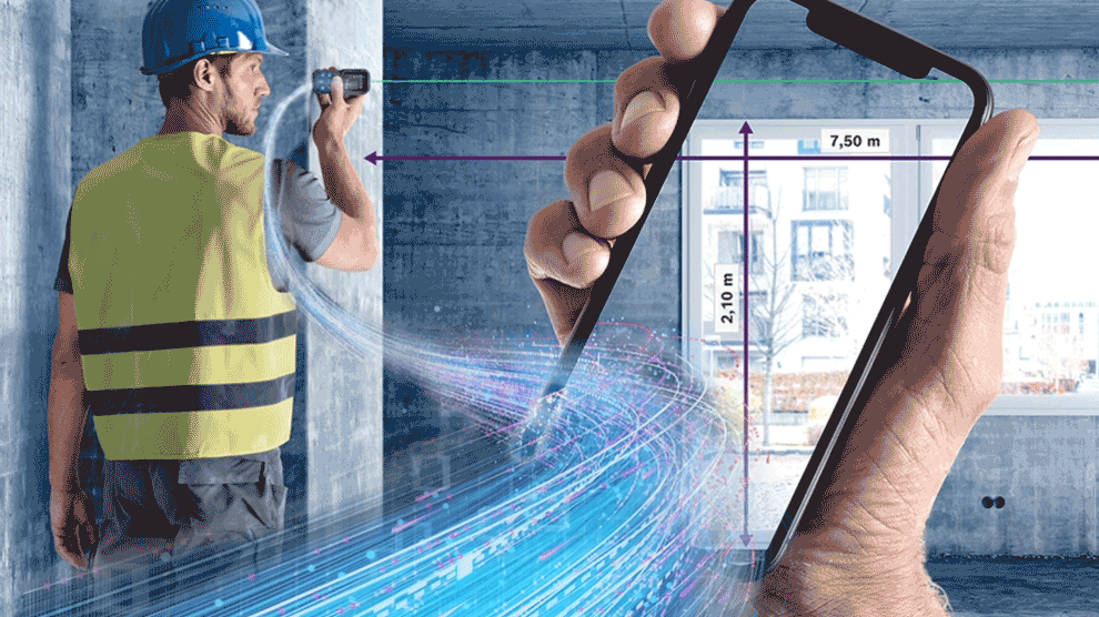 A craftsman in a yellow vest measures with a smartphone in a room.