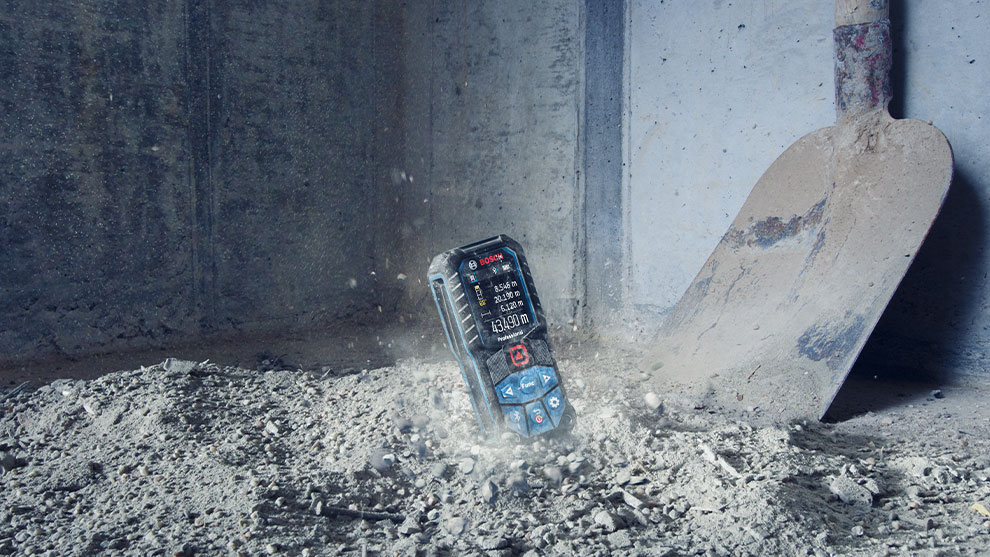 Bosch Professional laser distance measurer is lying on a dusty floor.