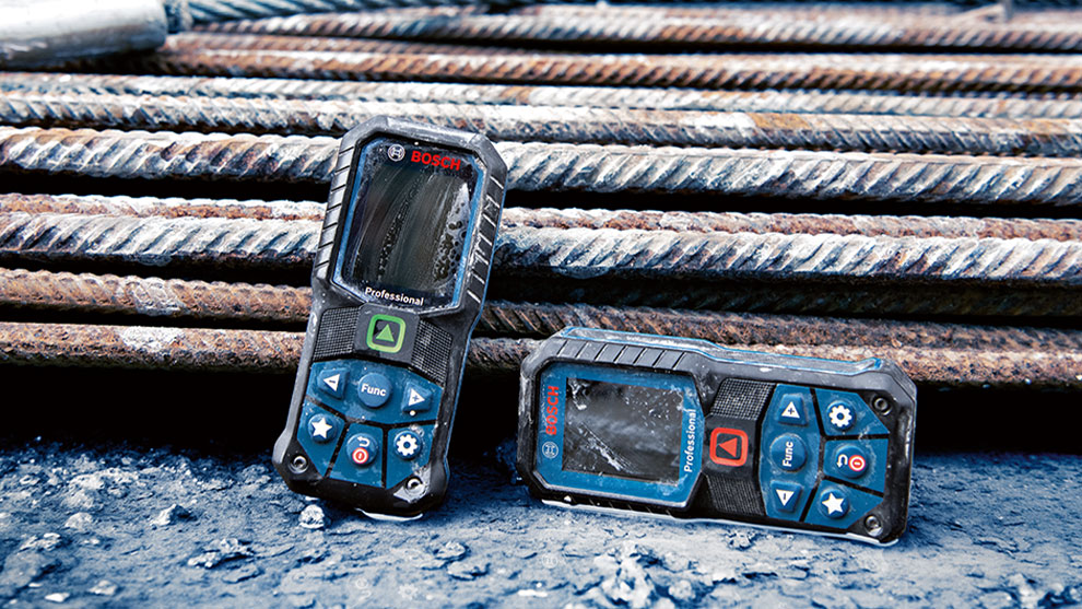 Two Bosch Professional measuring devices are lying on steel pipes.
