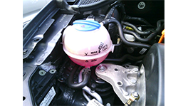 A pink coolant reservoir is located in the engine compartment of a car.
