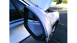 A silver side mirror of a car is damaged, hood open.