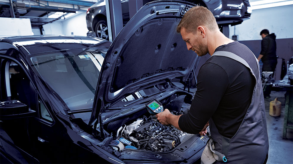 Mechanic checks engine with a diagnostic device in workshop.