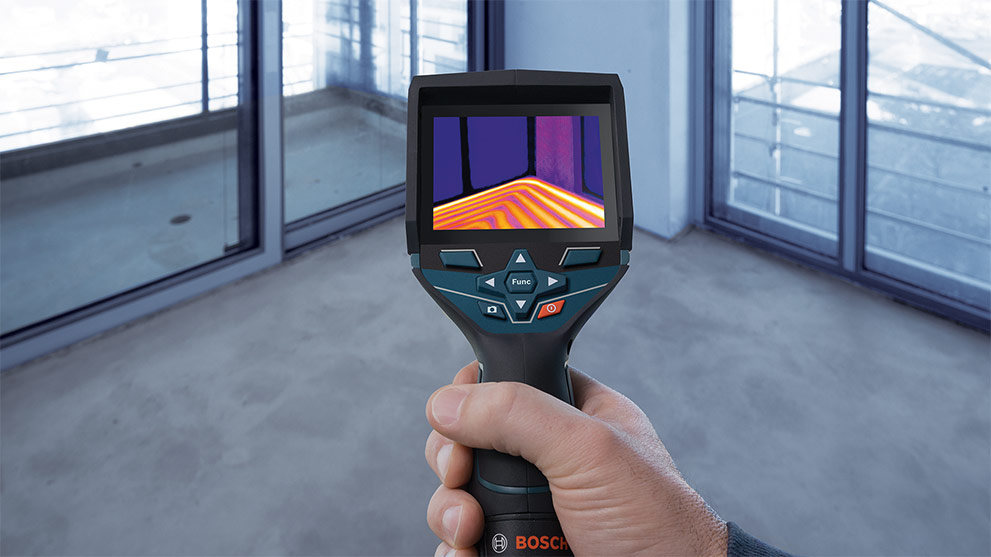 A hand holds a Bosch Professional thermal imaging device in a room.
