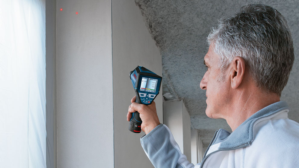 Man holds Bosch Professional laser device against wall, red glowing dots visible.