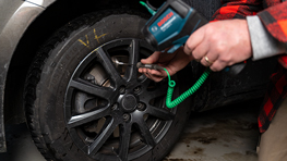 A person is using a Bosch Professional cordless screwdriver on a car tire.