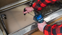 A person in a checkered shirt measures the temperature of a liquid.